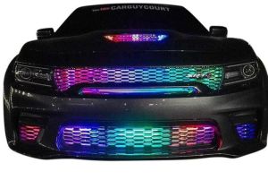 Front view of a black Dodge Charger SRT with a custom ColorChase LED grille kit, featuring vibrant RGB lighting across the upper and lower grille sections. The LED lights display a mix of red, blue, green, and purple colors, creating a dynamic and eye-cat